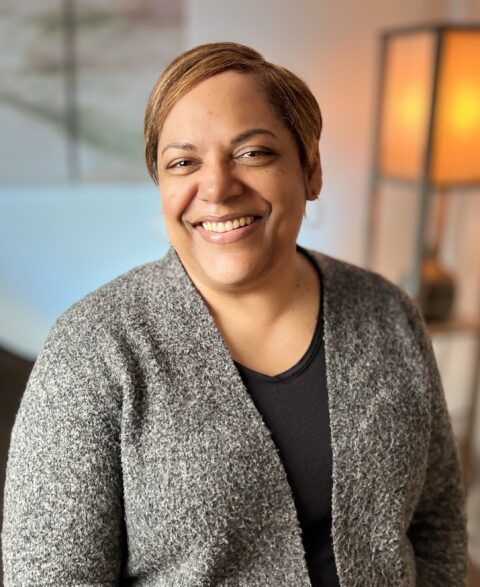 Lisa smiling broadly with a grey sweater over a black top