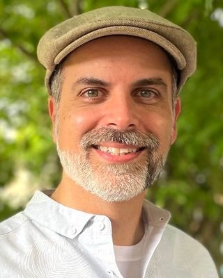 Paul smiling wearing a light collared shirt and a hat