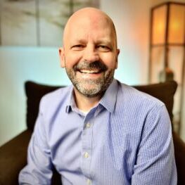 Dave-NEW-1-scaled Davis in a blue shirt smiling broadly at the camera